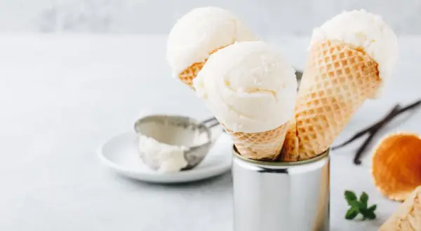 Cremiges griechischer joghurt eis ohne eismaschine in Waffelhörnchen. Ein Löffel und Vanilleschoten liegen daneben.