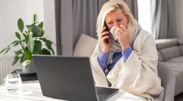 Chora kobieta owinięta kocem rozmawia przez telefon, trzymając chusteczkę.