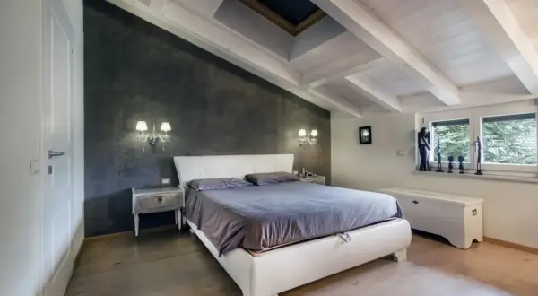 Camera da letto accogliente in un sottotetto non abitabile, con travi a vista, lucernario e pareti in resina.