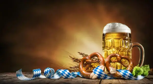 Boccale di birra dorata, pretzel e nastri bavaresi evocano la storia dell'Oktoberfest.