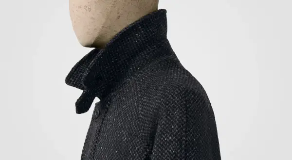 Dunkles Jackett mit hochgestelltem Kragen, der an ein Poloshirt erinnert. Das Material ist grob gewebt mit feinen roten Fäden.