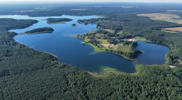 Malownicze jezioro Niesłysz otoczone lasami, z widocznymi wysepkami i zabudowaniami na brzegu.