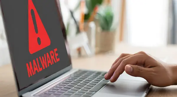 Czerwony wykrzyknik i napis "MALWARE" na ekranie laptopa, ostrzegający przed zagrożeniem, takim jak spyware.