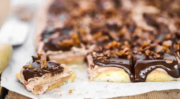 En bit av en chokladig snoddas kaka med fluffig kräm och chokladglasyr, toppad med krossad choklad och karamellbitar.