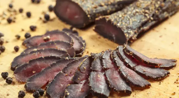 Tranches de filet mignon séché, assaisonnées de poivre noir, disposées sur une planche en bois.