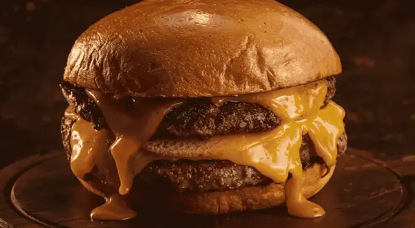 Gros plan sur un burger double au fromage fondant dégoulinant, sur un pain brioché doré.