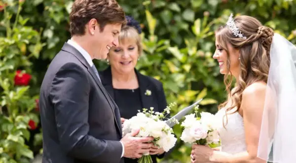 Cérémonie de mariage : une marraine émue lit une citation pour sa filleule rayonnante, entourées de fleurs.