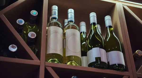 Butelki białego wina w drewnianym regale. Idealne miejsce, by dowiedzieć się, jak przechowywać wino, by zachowało swój smak.