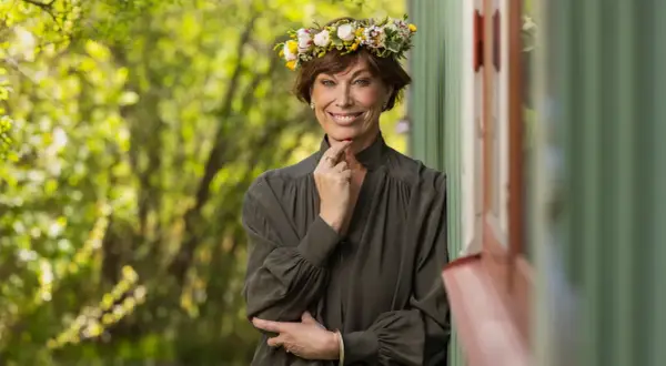 En kvinna med blomsterkrans ler mot kameran. Hon påminner om en sommarbild av mischa billing familj.