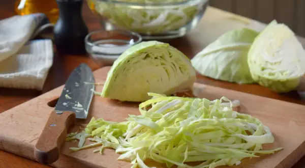 Frisch geschnittener Kohl liegt bereit für das Sauerkraut stampfen. Ein Messer und Gewürze sind auf dem Holzbrett arrangiert.