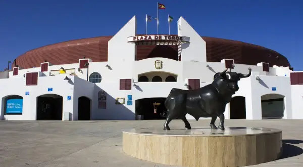 Escultura de toro frente a la Plaza de Toros Roquetas de Mar, bajo un cielo azul intenso.
