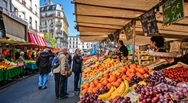 Frukt och grönsaksstånd på en livlig loppmarknad i Paris. Folk handlar bland färska druvor, apelsiner och tomater.