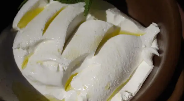 Kremowy ser labneh co to? Delikatny, biały ser z oliwą i miętą, podany w ceramicznej miseczce.