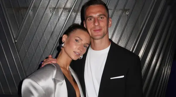 Agata Sieramska i jej partner pozują do zdjęcia. Ona ma na sobie srebrną marynarkę i dużą, metaliczną biżuterię.