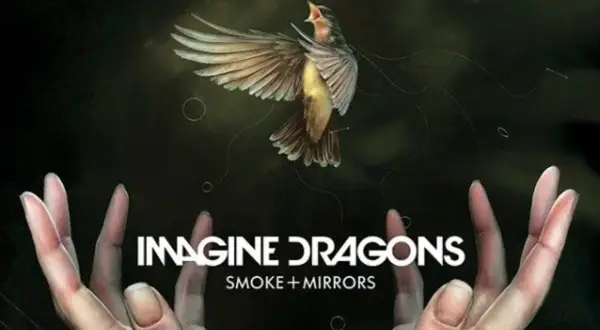 Ptak w locie nad dłońmi, z napisem "IMAGINE DRAGONS SMOKE + MIRRORS".