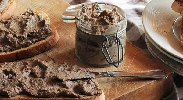 Des toasts tartinés de pâté, prêts à déguster. Un pot de crostini toscani et une assiette de crostini empilés complètent cette scène gourmande.