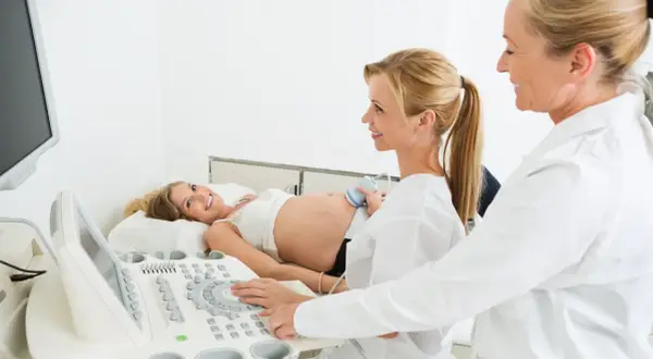 Lekarz ginekolog na NFZ wykonuje badanie USG ciężarnej pacjentki. Uśmiechnięta kobieta leży na kozetce, a lekarz obsługuje aparat.