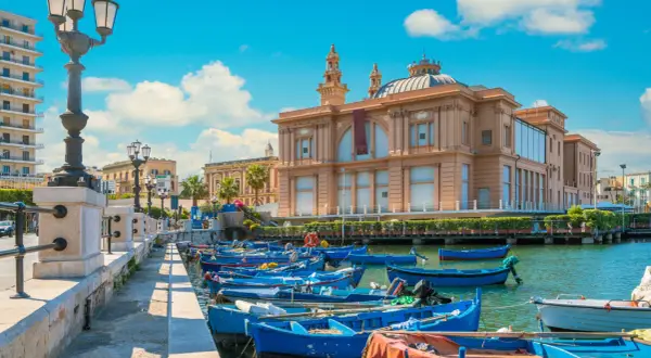 Barche blu ormeggiate nel porto, con il Teatro Margherita sullo sfondo. Un'immagine che cattura l'essenza di Bari e dintorni cosa vedere.
