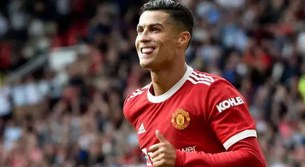 Cristiano Ronaldo w czerwonej koszulce Manchesteru United, z charakterystyczną fryzurą 2023, pokazuje kciuk w górę i wystawia język.