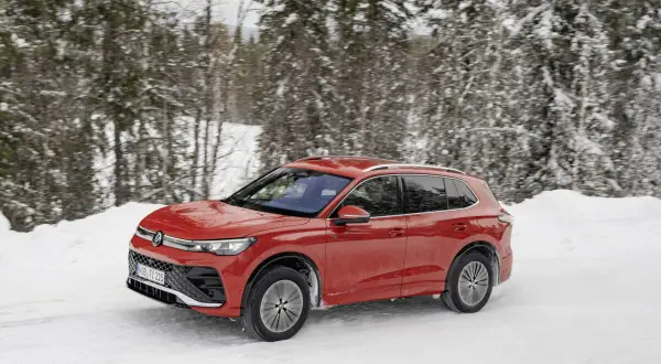 Czerwony Volkswagen Tiguan 5N pokonuje zasypaną śniegiem drogę w lesie.