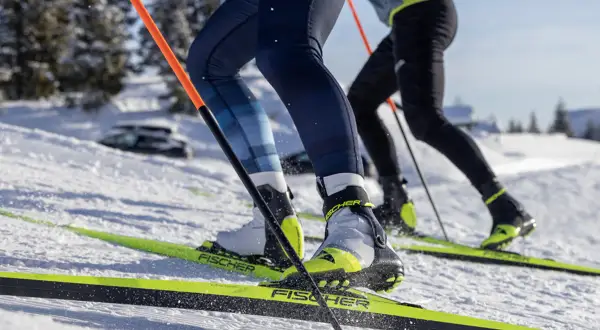 Zbliżenie na buty narciarskie i narty biegowe dwóch osób na ośnieżonym stoku.