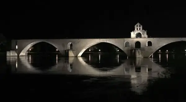 Nocna panorama na moście w Avignon. Kamienne łuki odbijają się w spokojnej wodzie rzeki Rodan.