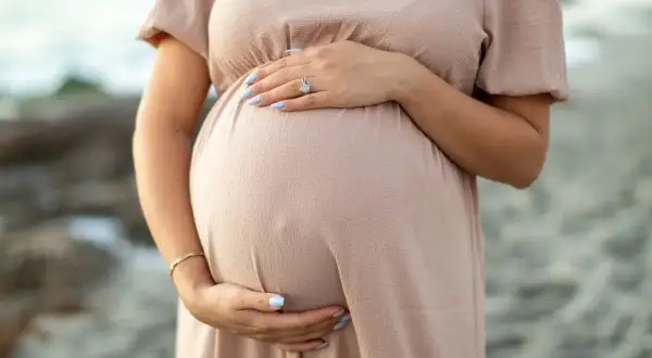 Brzuszek kobiety w ciąży, delikatnie otulony dłonią. W trosce o zdrowie maluszka, przyszła mama unika kosmetyków z **retinol w ciąży**.