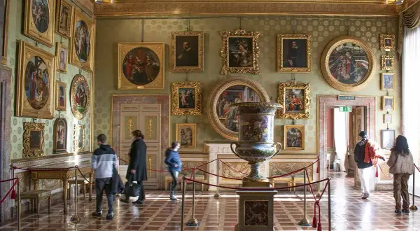 Interno di una sala del Palazzo Pitti, con opere d'arte alle pareti, un grande vaso e visitatori.