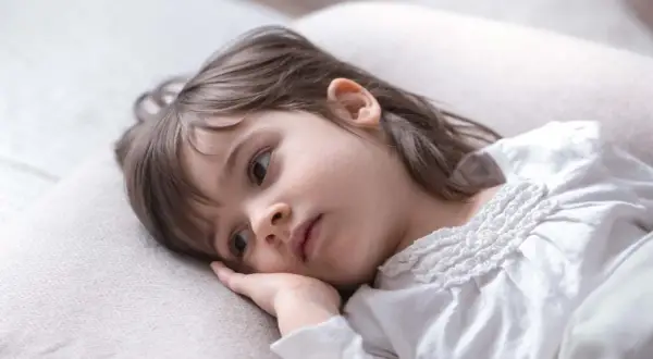 Smutna dziewczynka leży na poduszce, zamyślona. Może to oznaka problemów z zasypianiem u dziecka 7-letniego.