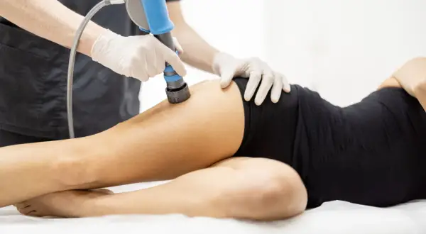 Therapeut führt maschinelle Lymphdrainage am Bein einer liegenden Person durch. Das Gerät hat einen blauen Griff.