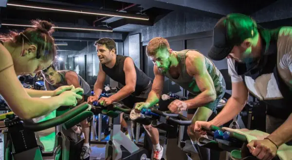 Intensywny trening spinningowy. Grupa ludzi pedałuje na rowerach stacjonarnych, skupiona na wysiłku.