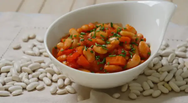 Schmackhafte weiße Bohnen in Tomatensoße, garniert mit Schnittlauch. Die Frage "wie lange bohnen kochen" wird hier visuell beantwortet: Sie sind perfekt gegart und servierfertig.