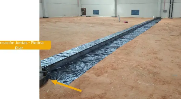 Instalación de una solera de hormigón con armadura metálica sobre plástico negro en interior de nave.