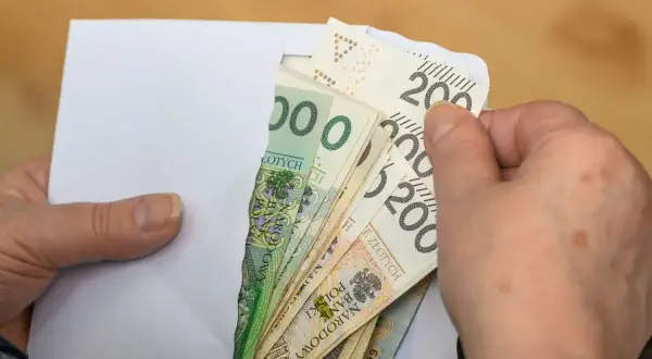 Dłonie wyciągają z koperty polskie banknoty. To może być pomoc finansowa, emerytura po mężu, czy oszczędności.