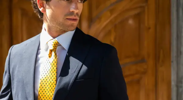 Uomo elegante con giacca blu, camicia bianca e cravatta gialla con pois, annodata con un perfetto nodo Windsor.