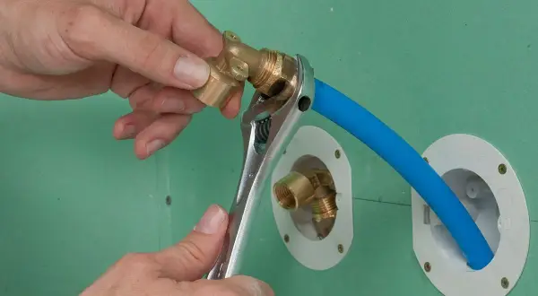 Installation d'un raccord pour l'arrivée d'eau de la douche. Une clé serre un coude en laiton sur un tuyau bleu.