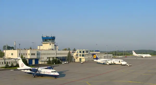 Lotnisko Katowice z wieżą kontroli lotów i samolotami na płycie. Które lotnisko większe Kraków czy Katowice?