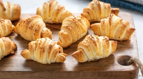 Croissant dorati su tagliere di legno, perfetti per una ricetta pasta sfoglia veloce.