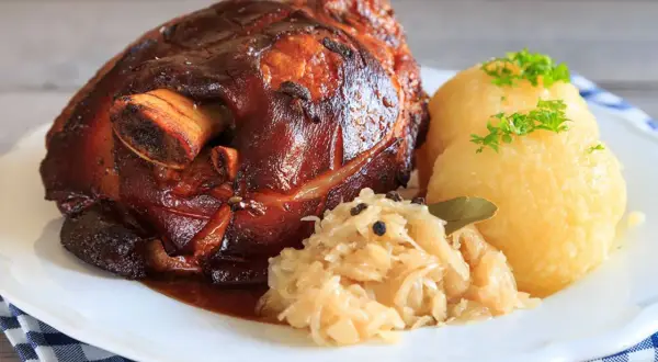 Knusprige Schweinshaxe mit Sauerkraut und Klößen, garniert mit Petersilie. Ein herzhaftes Gericht, das Appetit macht.