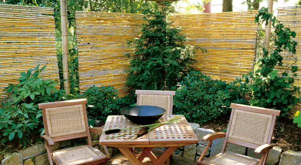 Ausgefallener Sichtschutz Garten selber machen: Bambusmatten und Holzmöbel schaffen eine gemütliche Ecke.