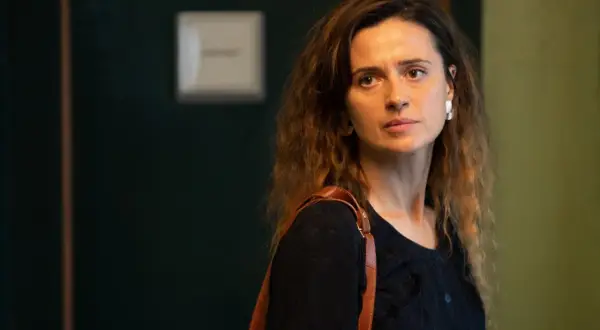 Agnieszka Grochowska, z brązową torbą na ramieniu, patrzy w bok zamyślona.