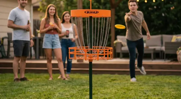 Vänner njuter av en inflyttningsfest med discgolf-lekar i trädgården. En man kastar en gul disc mot korgen.