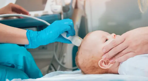 Lekarz wykonuje USG główki niemowlęcia, badając widoczny szew czołowy.