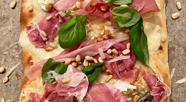 En läcker pinsa bianco med tunt skivad prosciutto, pinjenötter, färsk basilika och krämig ost.