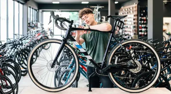 Ein junger Mann prüft ein schwarzes Fahrrad in einem Geschäft, um zu entscheiden, welches Fahrrad zu ihm passt. Viele Fahrräder stehen im Hintergrund.