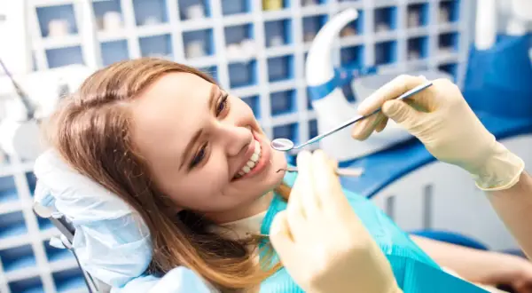 Uśmiechnięta kobieta u dentysty, badanie zębów lusterkiem i narzędziem.