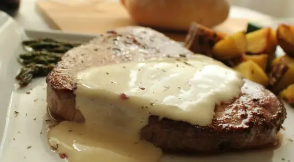 Filete redondo cubierto con una cremosa salsa blanca, acompañado de espárragos y patatas asadas.
