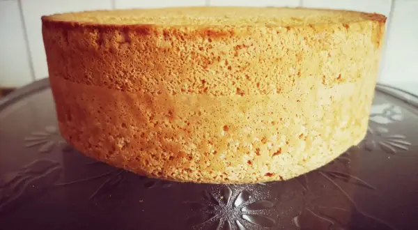 En gyllene anslag tårta med en porös textur står på ett mönstrat fat. Den är redo att dekoreras för ett speciellt tillfälle.