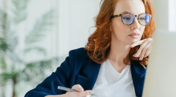 Kobieta w okularach z modną oprawką pracuje przy laptopie. Dofinansowanie do okularów może pomóc w zakupie stylowych i wygodnych oprawek.