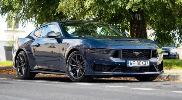 Nowy Ford Mustang 2025 w ciemnoniebieskim kolorze, zaparkowany pod drzewem.